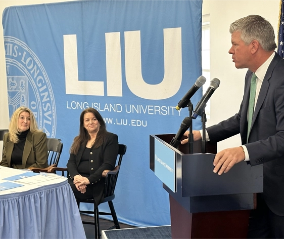 a man speaking at a podium with two women watching