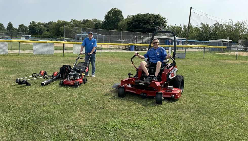 East Meadow Little League Inaugural Mow participants with ride-on mowers on baseball field.